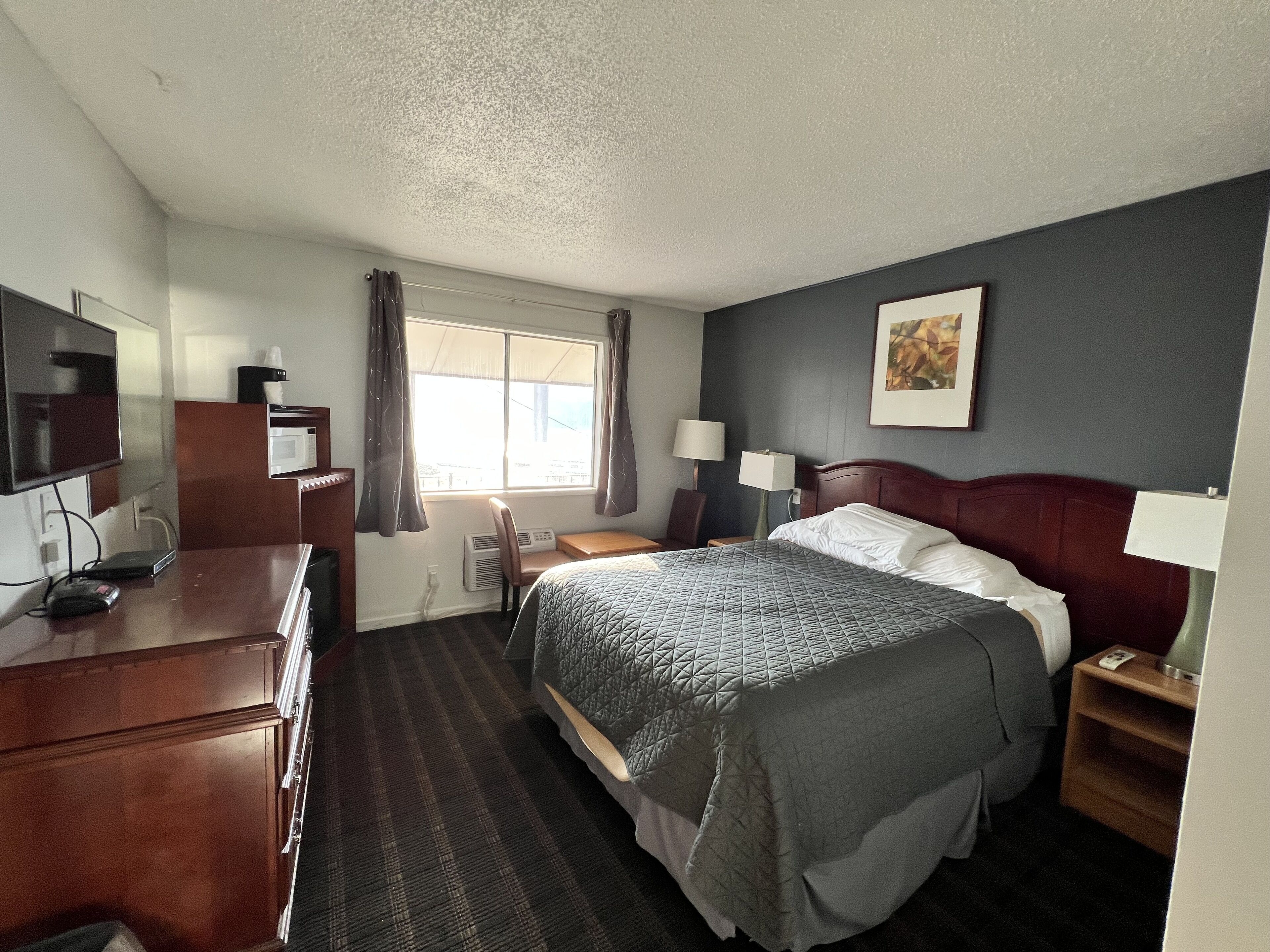 A hotel room with a bed, a desk, a chair, a TV, and a window with curtains.