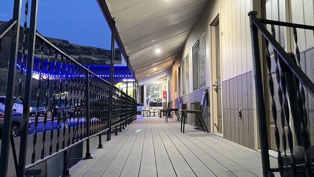 A covered outdoor area with a wooden deck, metal railings, and a building entrance. - BIGGS NU-VU MOTEL (Biggs Junction)