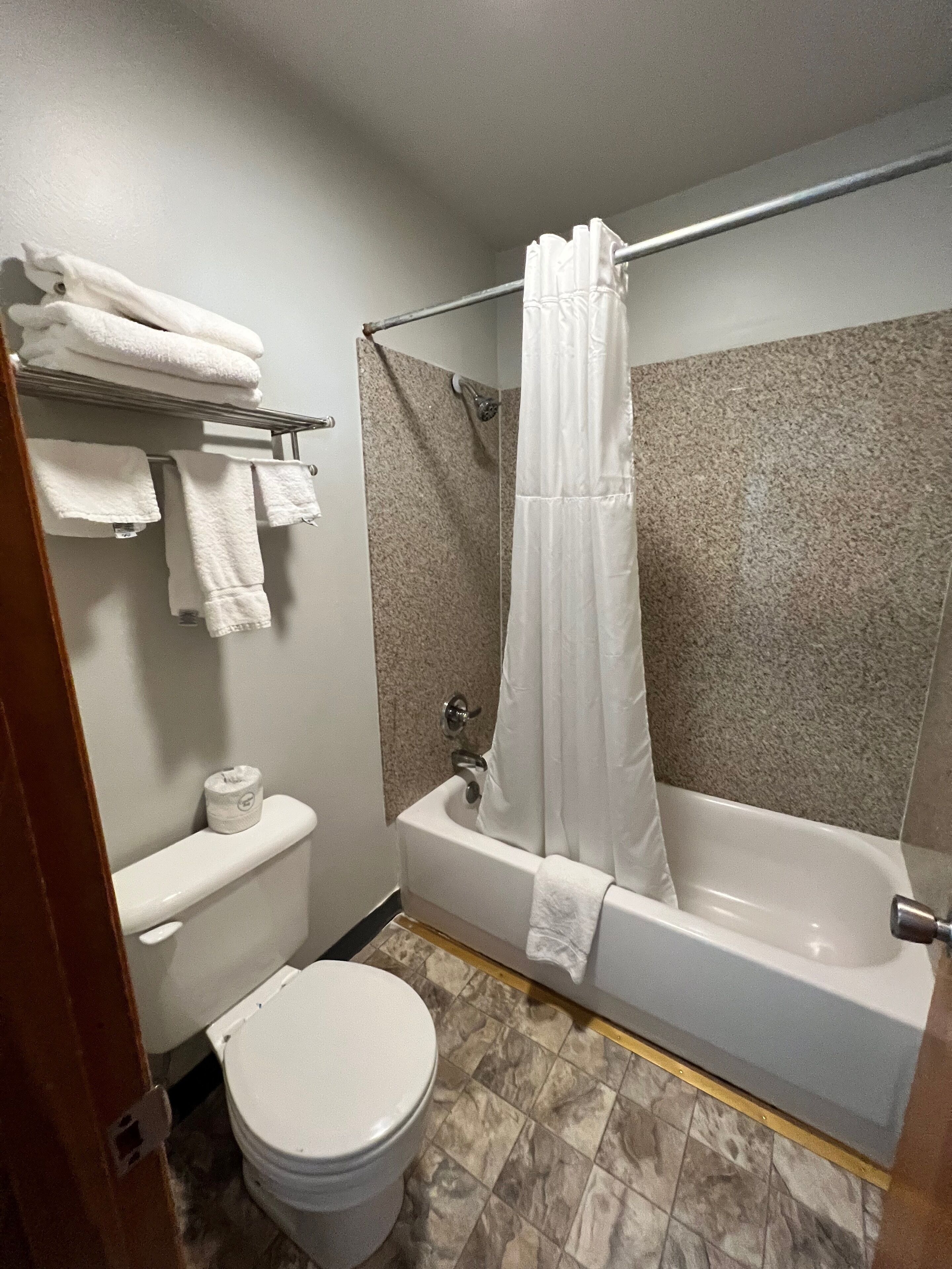 A bathroom with a toilet, a bathtub with a shower curtain, and a towel rack with folded towels.