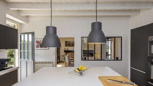A modern kitchen with two pendant lights, a central island with a cutting board and knife, and a dining area visible through an open door.