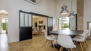 A modern dining area with a large table and white chairs, a sliding door, and a hanging industrial-style light fixture.