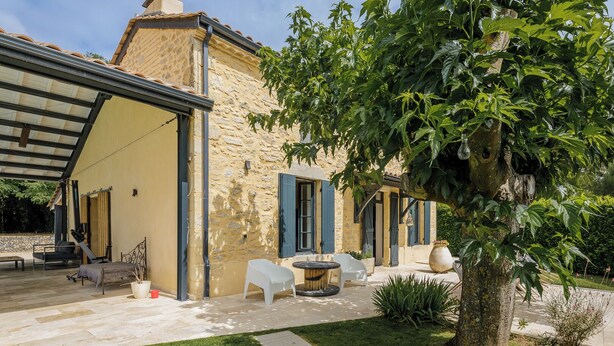 A stone building with a covered patio area, outdoor seating, and a tree.