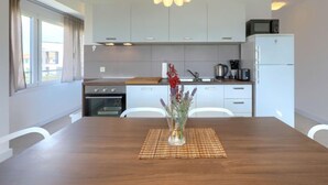 Una cucina moderna con mobili bianchi, un forno a microonde, un frigorifero e un tavolo da pranzo con un vaso di fiori.