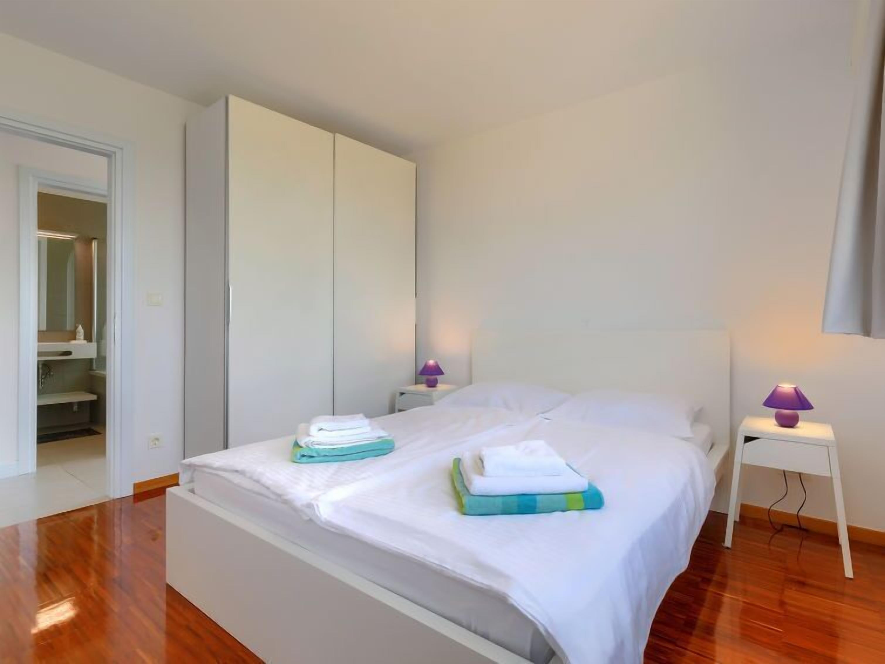 A bedroom with a bed, two bedside tables, a wardrobe, and a bathroom visible through an open door.