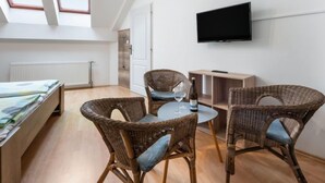 Ein modernes, helles Zimmer mit einem Bett, zwei Korbstühlen, einem kleinen runden Tisch und einem Fernseher an der Wand.