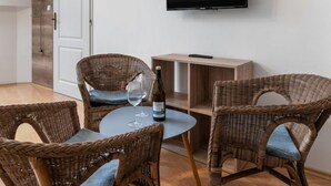 Ein Zimmer mit Rattanmöbeln, einem an der Wand befestigten Fernseher und einer Weinflasche auf dem Tisch.
