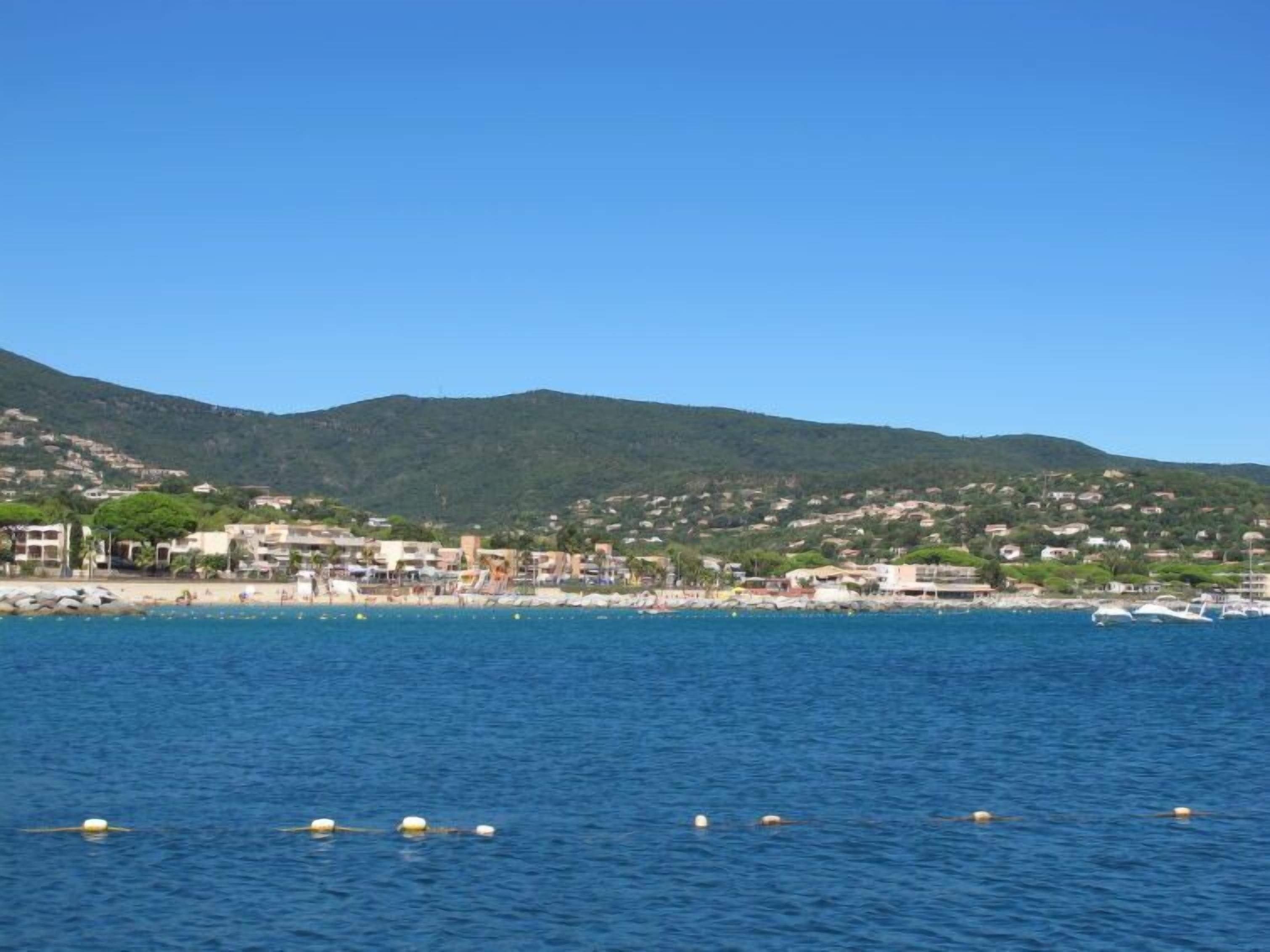 A coastal town with buildings along the shore, a clear blue sky, and boats in the water.