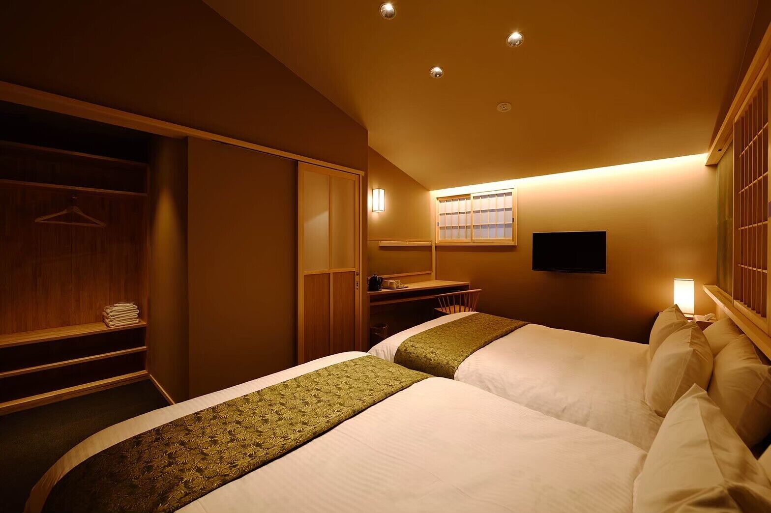 A hotel room with two beds, a desk, a wardrobe, and a TV.