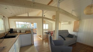 A spacious living area with a wooden floor, a grey sofa, and a kitchen area with a sink and cabinets. - Authentic wooden chalet with sea view sleeps 4 (Gruissan)