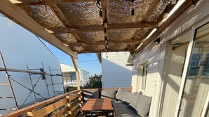 A wooden deck with a sofa and table, a pergola overhead, and a view of the sea. - Authentic wooden chalet with sea view sleeps 4 (Gruissan)