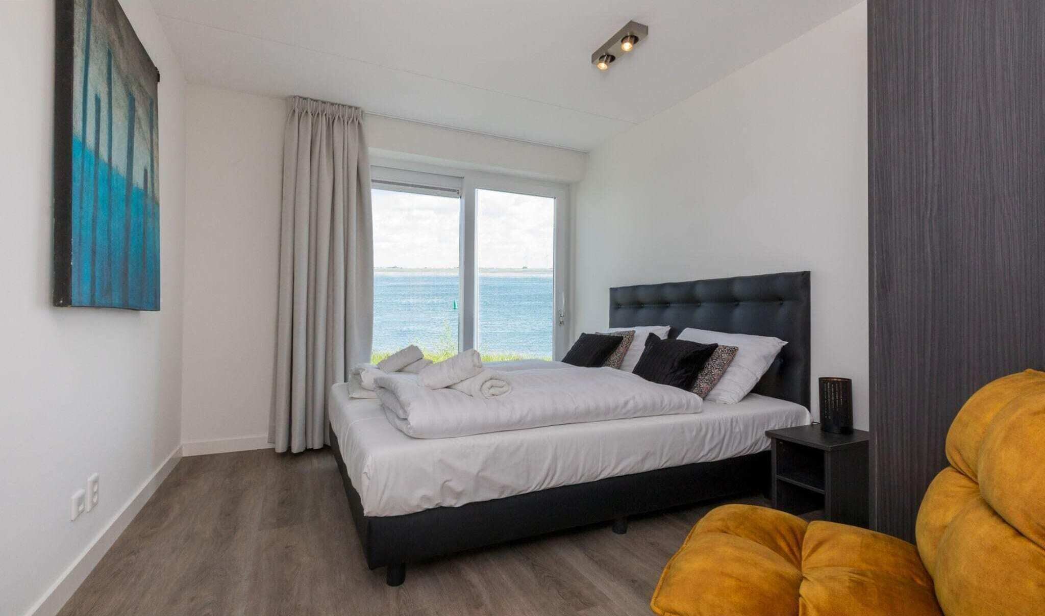 Een slaapkamer met een groot bed, uitzicht op de zee door het raam, en een schilderij aan de muur.