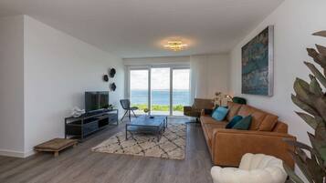 Een moderne woonkamer met een televisie, zitplaatsen en uitzicht op zee.