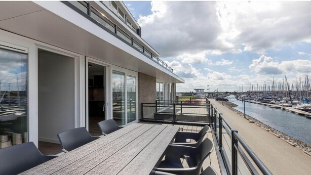 A modern building with a dining area overlooking a marina with boats.
