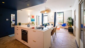 A modern kitchen with a central island, a dining area with chairs, and a large window providing natural light. - Roma Divine: home cinema, luxury city center (Nimes)