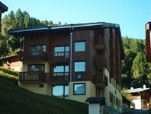 A multi-story building with balconies, large windows, and a sloped roof.