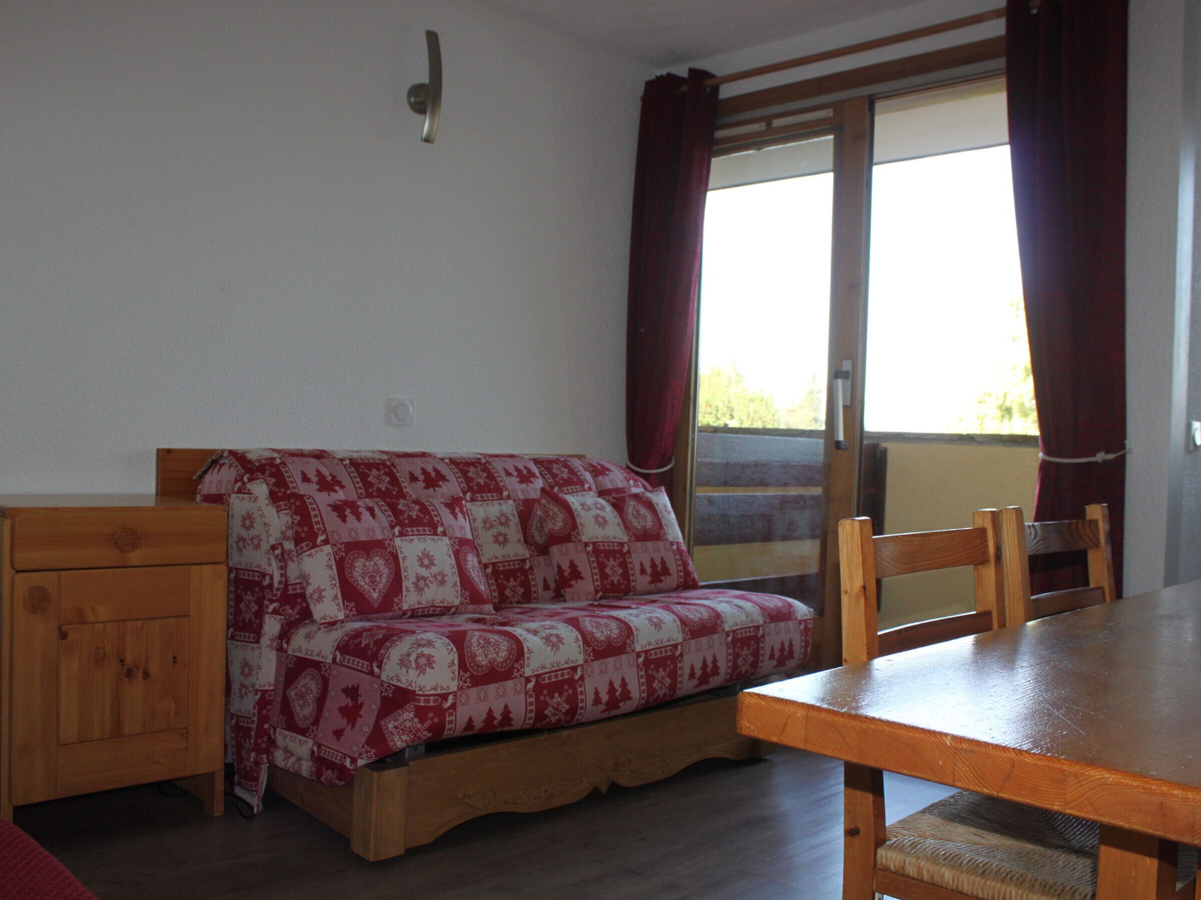 A cozy room with a wooden bed, a wooden table, and a window with curtains.