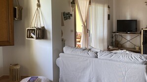 A cozy room with a wooden ceiling, a bed with white bedding, a television on a stand, and a small round ottoman with a book.