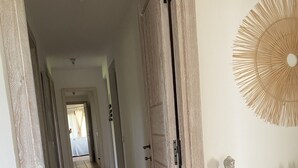 A hallway with a wooden door, a woven wall hanging, and a small table with decorative items.