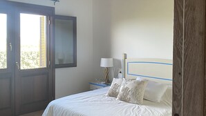 A bedroom with a wooden ceiling, a bed with white bedding, a nightstand with a lamp, and a door leading to an outdoor area.