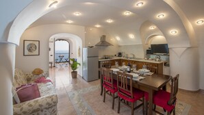 A spacious kitchen with an arched ceiling, a dining area with red chairs, and a view of the sea through an open archway.