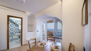 A dining area with a wooden table set for two, chairs, and a view through an open door to a bathroom with blue and yellow tiles.