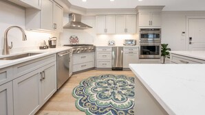 Una cucina moderna con mobili bianchi, elettrodomestici in acciaio inossidabile e un tappeto decorativo.