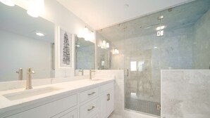A modern bathroom with two sinks, a large mirror, and a glass-enclosed shower.