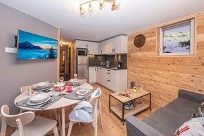 A modern kitchen with white cabinets, a dining area with a round table set for four, and a living area with a sofa and a coffee table.