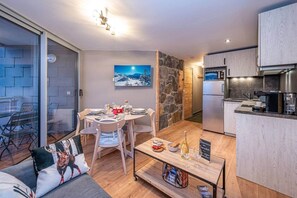 A modern living room with a dining area, a kitchen, and a stone wall.