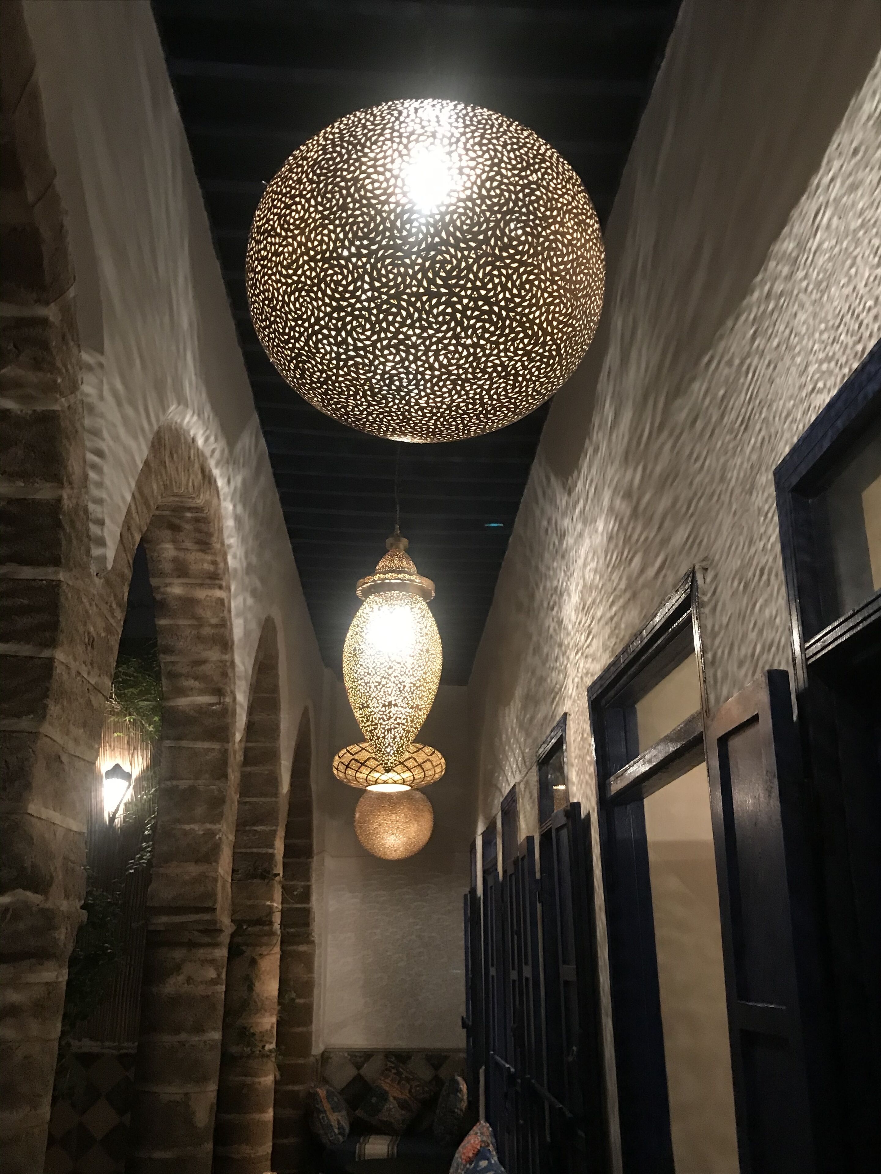 A corridor with arched ceilings, a hanging spherical light fixture, and a seating area with cushions.