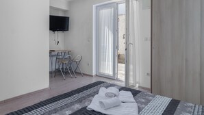 Un dormitorio con cama, escritorio y sillas, televisor y puerta corrediza de vidrio a un espacio exterior.