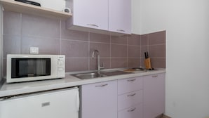 Una cocina compacta con un microondas blanco, un lavamanos y un bloque de cuchillos.