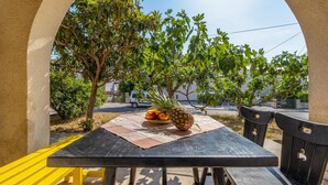 Una mesa al aire libre con una piña y un plato de frutas, rodeada de árboles y bancos.