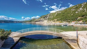 Vista despejada de una zona costera con un puente sobre aguas tranquilas, rodeada de colinas y un puerto deportivo con barcos.