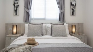 A modern bedroom with a large bed, two bedside tables with lamps, and abstract wall art.
