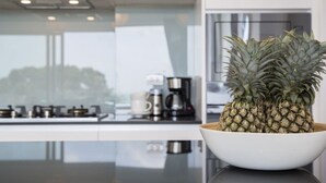 A modern kitchen with a large island, a coffee maker, and a bowl of pineapples.