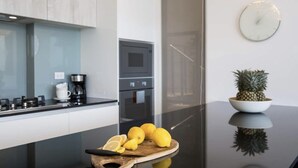 A modern kitchen with a black countertop, a wooden cutting board with lemons, a pineapple, and a coffee maker.
