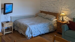 Une chambre à coucher avec un lit, une télévision, une lampe et un mur en pierre.
