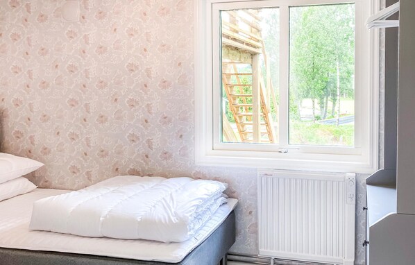 A bedroom with a bed, a radiator, and a window with a view of a wooden structure and trees.