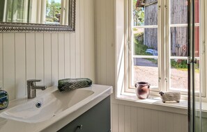 Ein Badezimmer mit einem weißen Waschbecken, einem Spiegel und einem Fenster mit Blick ins Freie.