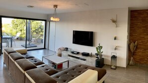 A modern living room with a large TV, comfortable seating, and a sliding glass door leading to an outdoor area.