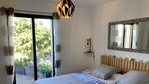 A bedroom with a large bed, a wooden headboard, a mirror, and a view of greenery outside.