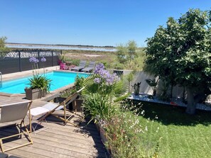 A backyard with a swimming pool, lounge chairs, and a wooden deck. - Villa Avec Piscine, vue Magnifique sur la Camargue (Le Grau-du-Roi)
