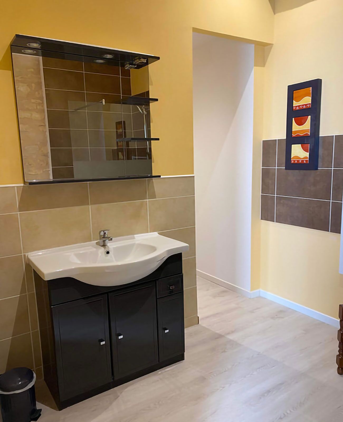 Un baño moderno con lavamanos blanco, muebles oscuros, cabina de ducha con mampara de cristal y azulejos decorativos en la pared.