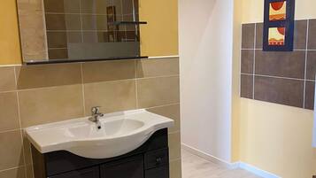 Un baño moderno con lavamanos blanco, muebles oscuros, cabina de ducha con mampara de cristal y azulejos decorativos en la pared.