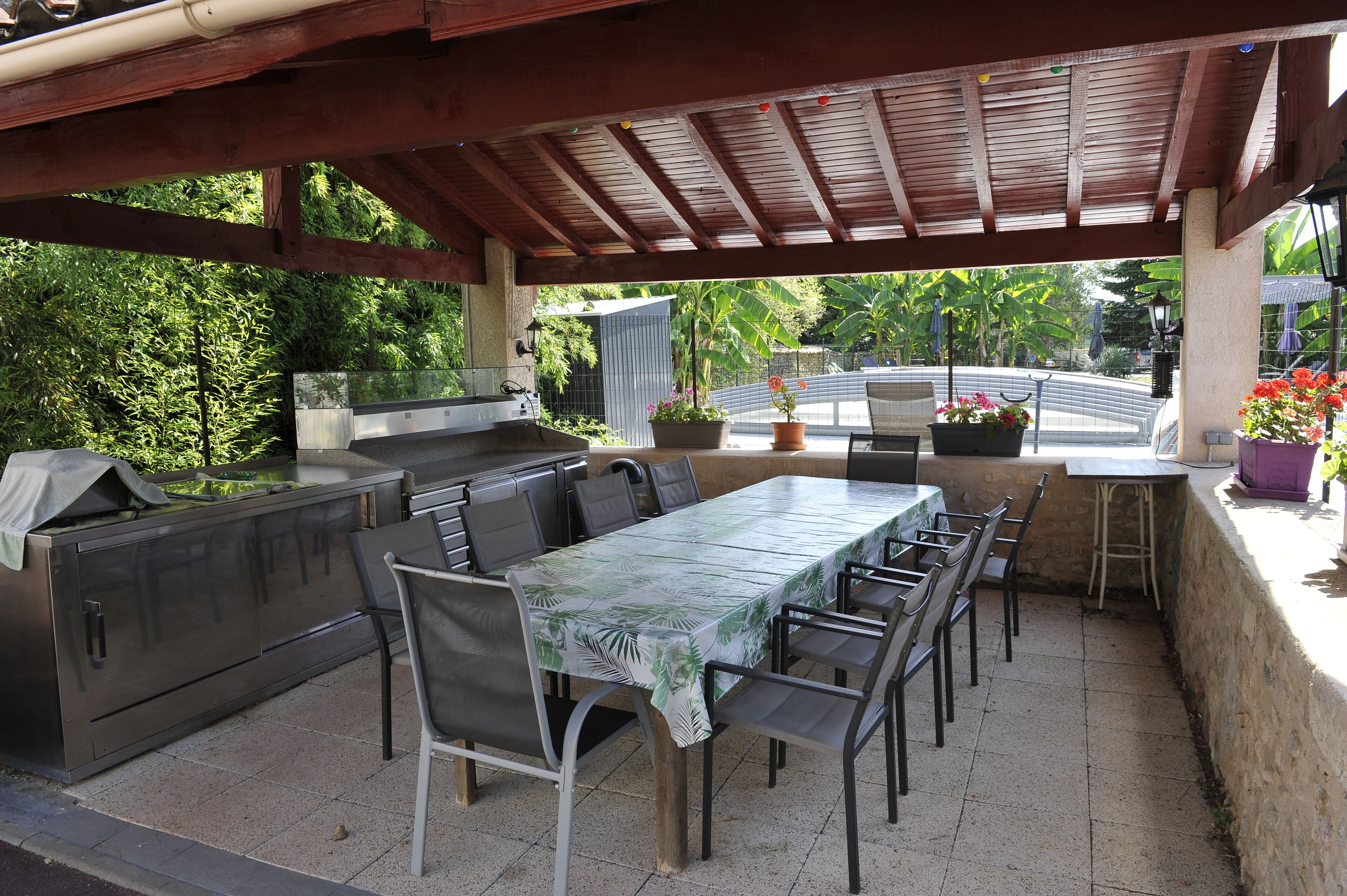 Eine Terrasse im Freien mit überdachter Essgegend, Grill und Blumentöpfen.