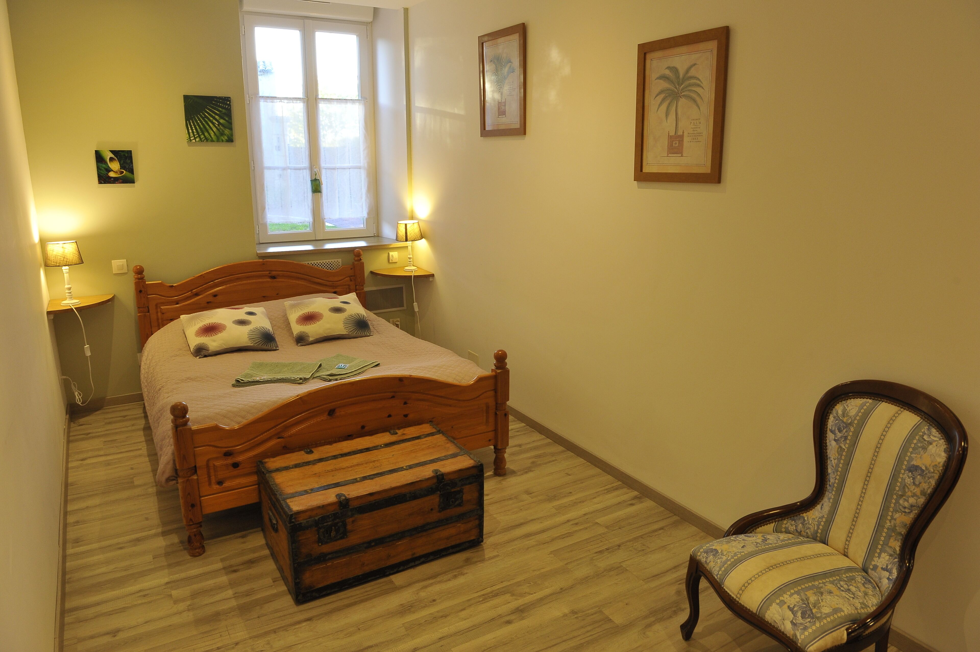 Une chambre à coucher avec un lit en bois, deux lampes de chevet, une fenêtre, une chaise et une valise.