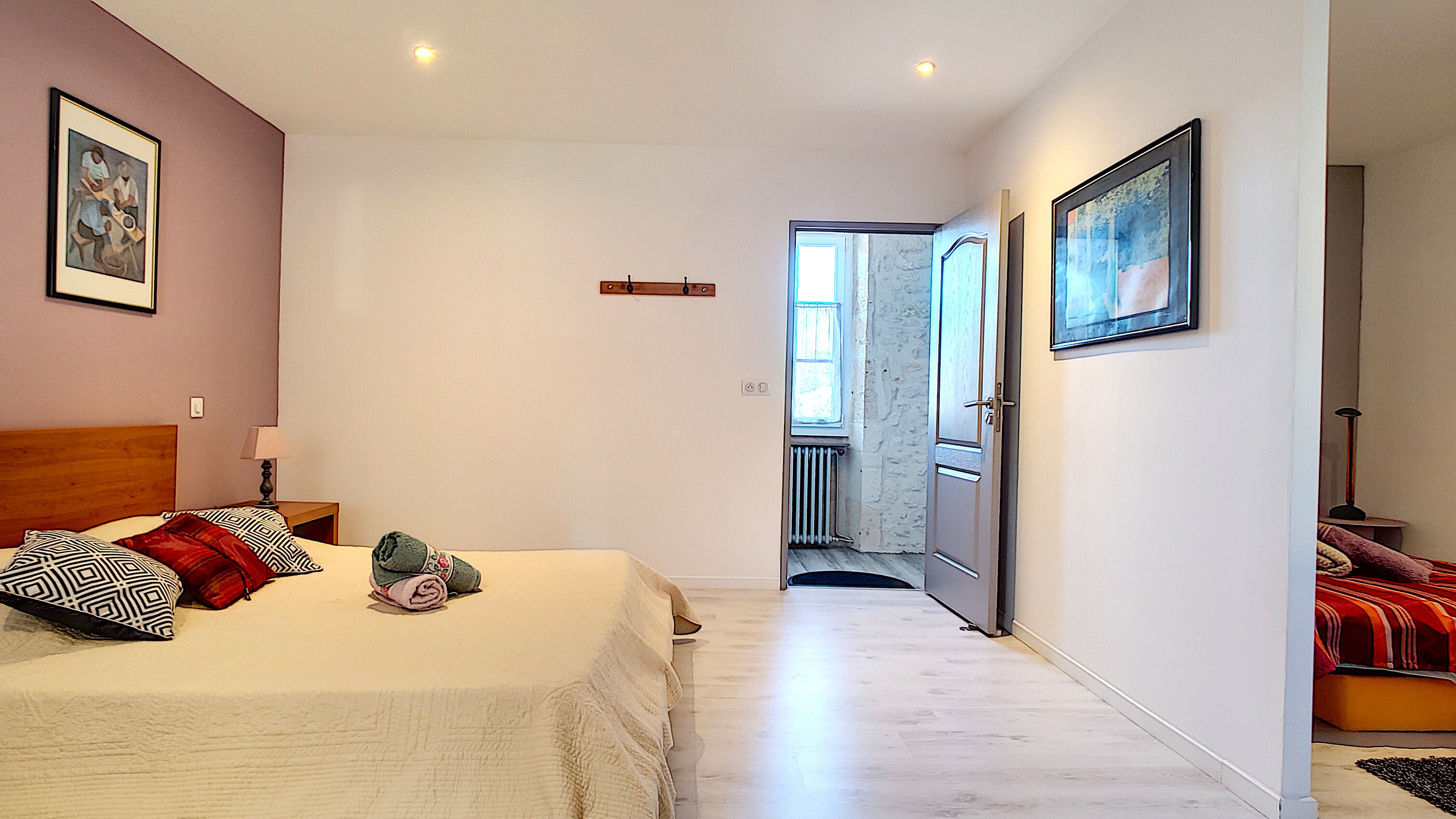 A bedroom with a bed, pillows, a nightstand, a lamp, a door leading to a balcony, and a framed picture on the wall.