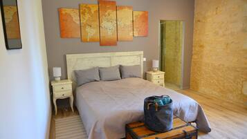 A neatly made bed with a light-colored headboard, a world map on the wall, and a suitcase on the floor.