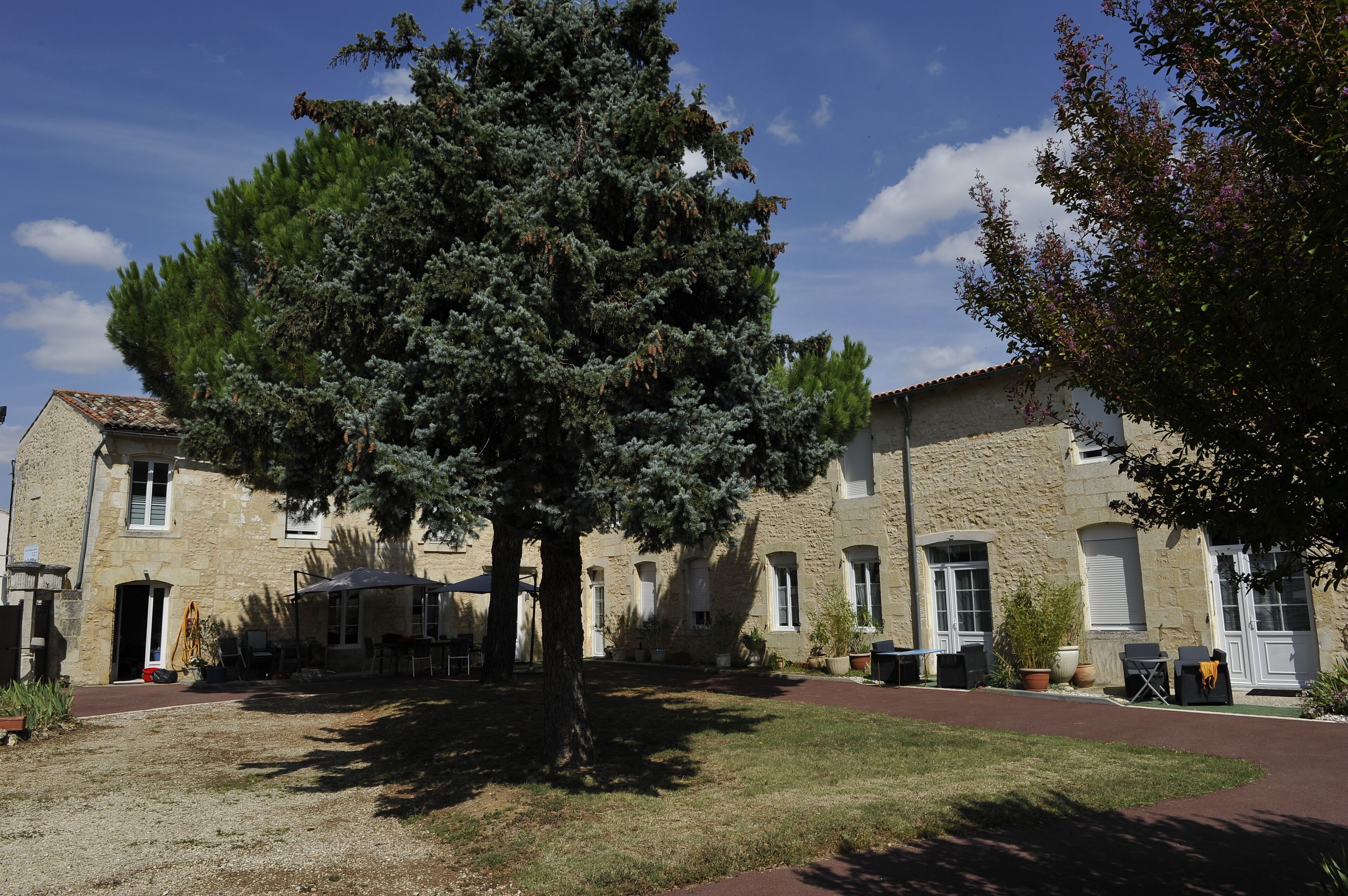 A stone building with a large tree in front, outdoor seating, and a clear sky.